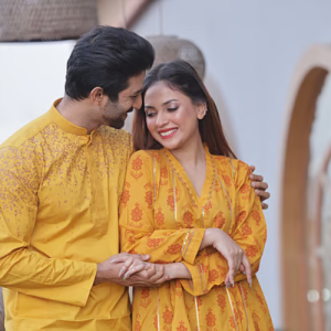 Both are wearing Basanti colored clothes. Anarkali style kameez is dominated by red color block design and thin lace of zari. It is like the manifestation of both spring and love. Color is key in Punjabi designs